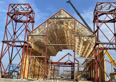 Commercial roof framing under construction, rows of newly set wood trusses spanning the structure with a crane on site.